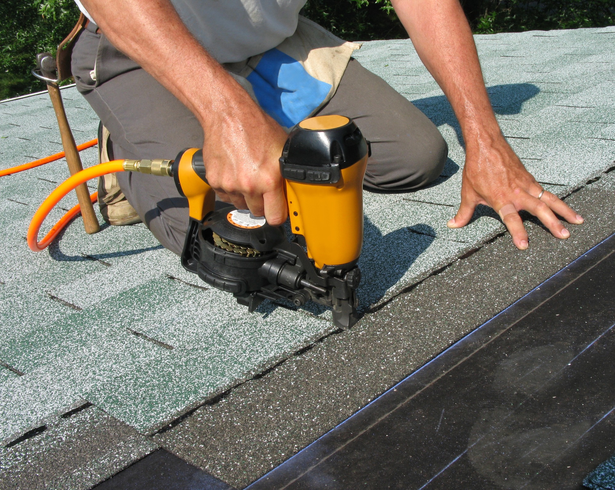 A worker uses a pneumatic nail gun to install shingles on a roof